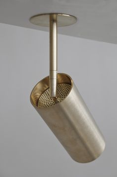 a brass colored light fixture with a metal cup hanging from it's side and a white wall in the background