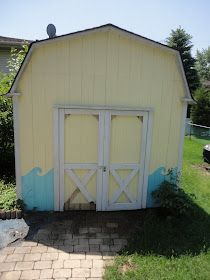 a yellow and blue shed sitting on top of a grass covered field next to a brick walkway