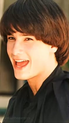 a close up of a person wearing a black shirt and smiling at the camera with a building in the background