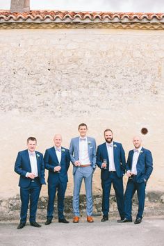 a group of men standing next to each other in front of a stone wall and wearing suits