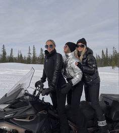 two women standing next to a snowmobile in the snow with one woman wearing sunglasses