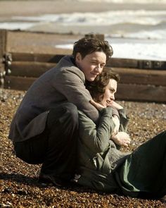 two people are sitting on the beach and one is holding another person's back