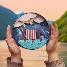 a person holding up a paper plate with an image of a boat in the water