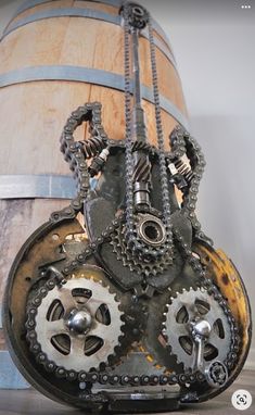 an old clock with gears attached to it sitting on top of a wooden barrel next to a chain