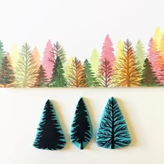 three felt trees sitting on top of a table next to a colorful forest wall hanging