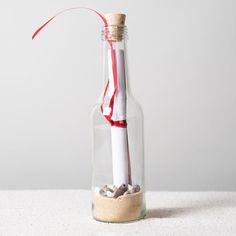 an empty glass bottle filled with sand and a red straw sticking out of the top