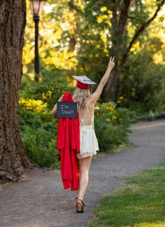 a woman in a graduation cap and gown walks down a path with her arms up