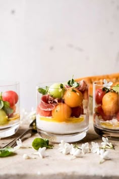 three glasses filled with fruit and garnish on top of a white tablecloth