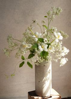 a vase filled with white flowers sitting on top of a wooden block