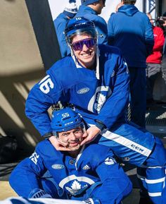 two men in blue hockey uniforms sitting next to each other on the side of a building