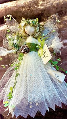 a white angel with pine cones and greenery on it's wings, holding a tag