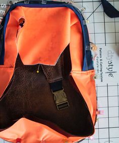 an orange and blue backpack sitting on top of a cutting board next to some scissors