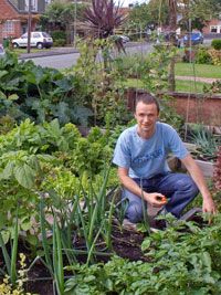 a man kneeling down in the middle of a garden filled with lots of green plants