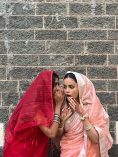 two women standing next to each other in front of a brick wall and covering their faces