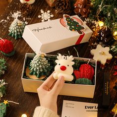 someone is holding a small christmas ornament in a box with other ornaments around it