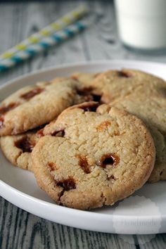 three chocolate chip cookies on a white plate with a glass of milk in the background