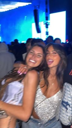 two beautiful women standing next to each other in front of a crowd at a party