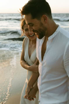 a man and woman walking on the beach holding each other's hands while smiling