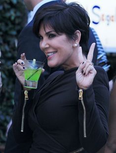 a woman holding a drink in her right hand and making the peace sign with her left hand