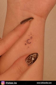 a woman's hand with a small tattoo on her left wrist and the moon behind it