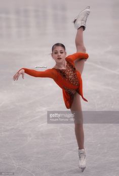 a female figure skating on an ice rink with her arms in the air and one leg up