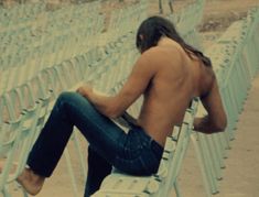 a shirtless man sitting on top of a white chair in front of rows of chairs