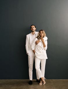 a man and woman dressed in white standing next to each other against a gray wall