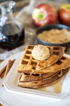 a stack of waffles on a plate with apples and cinnamon sticks in the background