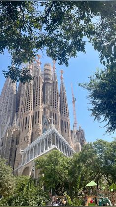 the building is very tall and has many spires on it's sides in front of some trees