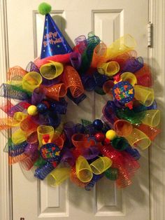 a colorful mesh birthday wreath hanging on a door with a happy birthday hat on it