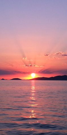 the sun is setting over the ocean with mountains in the distance and water below it