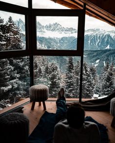 two people sitting on the floor in front of a window looking out at snow covered mountains