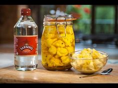 a wooden table topped with glass jars filled with food next to a bowl of macaroni and cheese