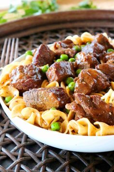 a white bowl filled with pasta and meat on top of a wooden table next to a fork