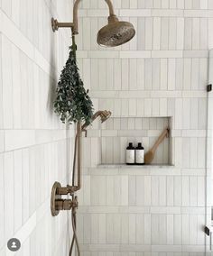 a bathroom with white tiled walls and flooring, including a shower head and hand held faucet