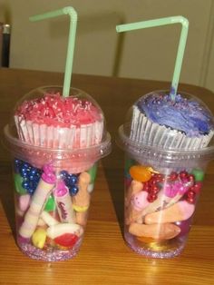 two plastic cups filled with cupcakes and candy on top of a wooden table