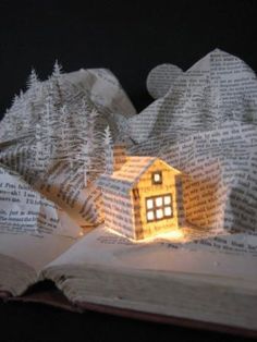 an open book with a house made out of pages and lights on top of it