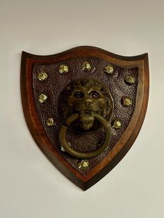 a metal lion head mounted to the side of a wooden shield on a white wall