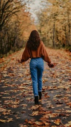 a woman walking down a leaf covered road