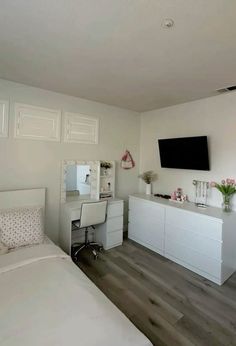 a bedroom with white furniture and a flat screen tv mounted on the wall above it