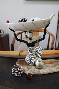 a ceramic figurine holding a surfboard on top of a wooden table next to pine cones