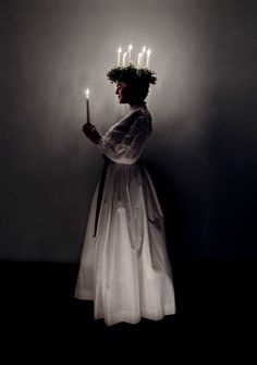 a woman in a white dress holding a candle and wearing a wreath of flowers on her head