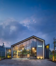 a modern building with glass walls and lights on the outside, at dusk or dawn