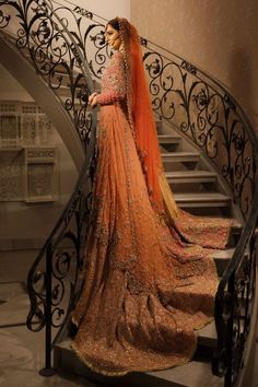 a woman in an orange and gold wedding dress standing at the top of a staircase