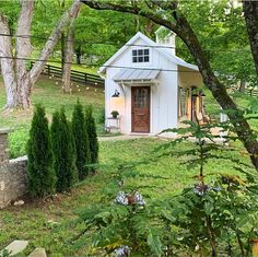 a small white house sitting in the middle of a lush green field next to trees