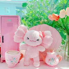 a pink stuffed animal sitting next to a cup and vase with flowers in it on a table