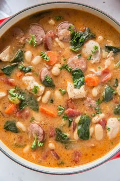 a bowl of soup with meat, beans and spinach on the side next to a spoon