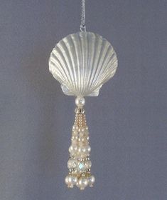 a sea shell ornament with pearls hanging from it's side on a chain