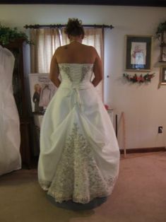 a woman in a white wedding dress looking at herself in the mirror with her back to the camera