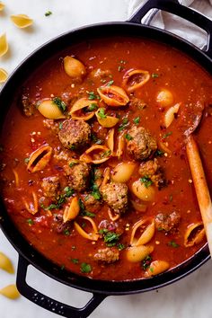 a pan filled with pasta and meatballs on top of a white table next to noodles